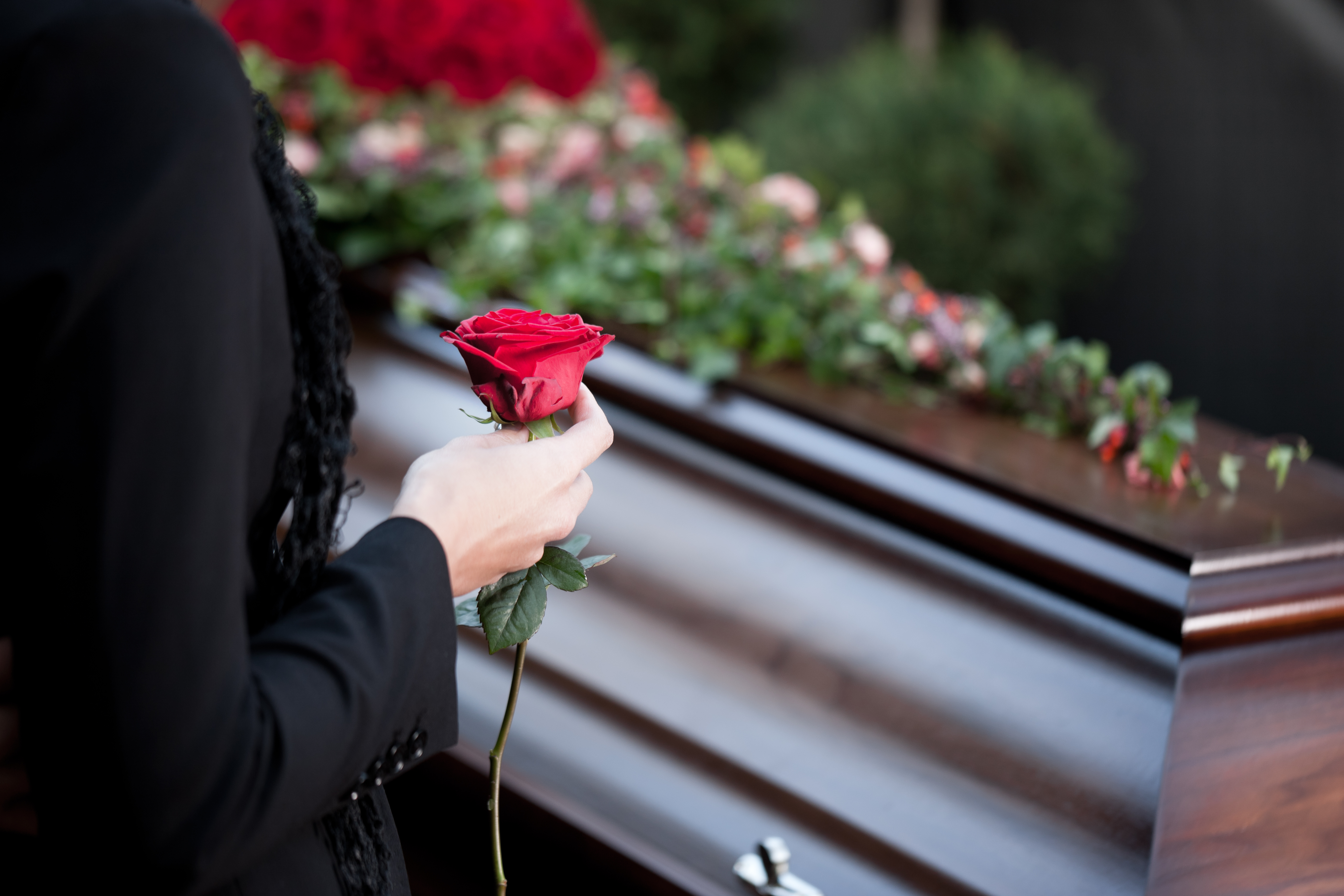 woman holding rose next to coffin
