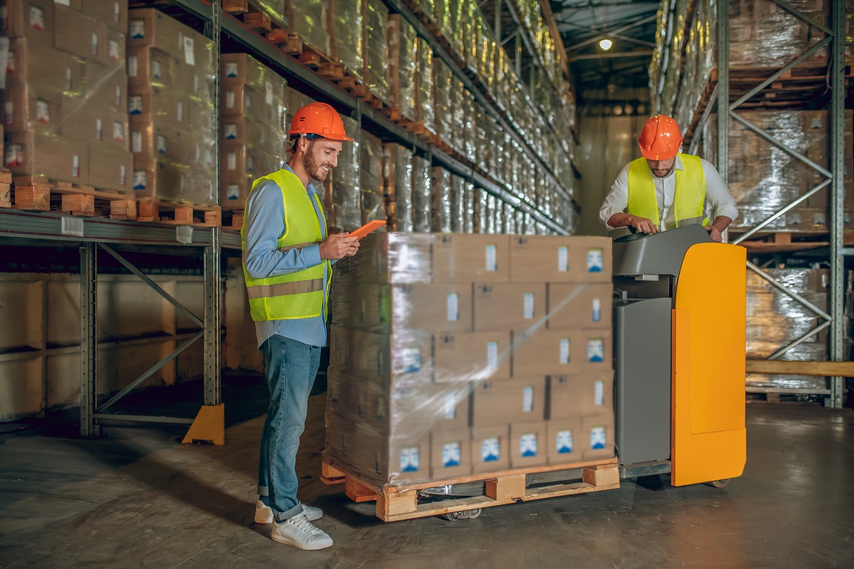 Warehouse workers wearing helmets and neon vests while checking inventory